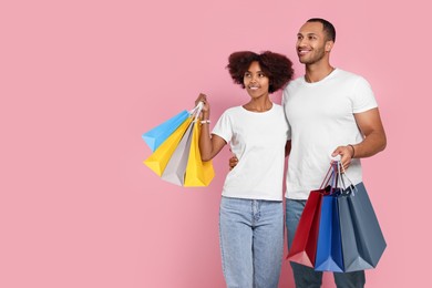 Happy African American couple with shopping bags on pink background. Space for text