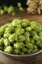 Photo of Fresh green hops in sieve on wooden table, closeup