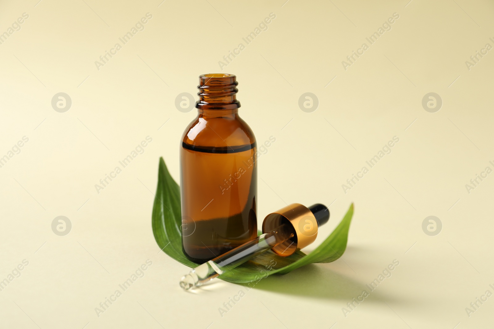 Photo of Bottle of cosmetic oil, pipette and leaf on beige background