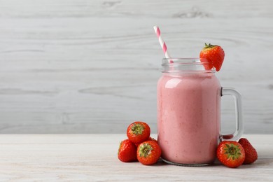 Photo of Mason jar with delicious strawberry smoothie and fresh berries on white wooden table. Space for text