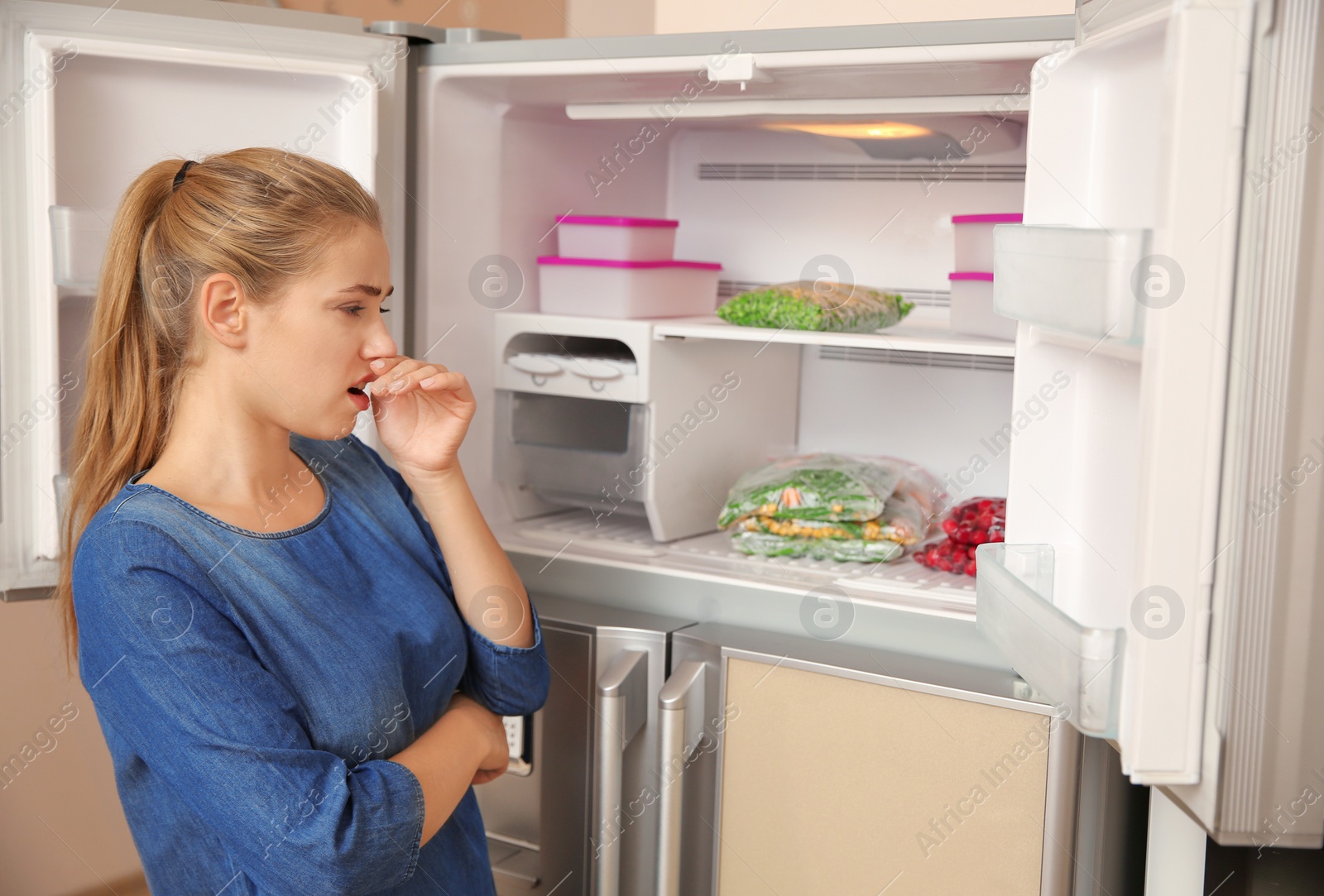 Photo of Young woman holding nose cause of bad smell in refrigerator at home