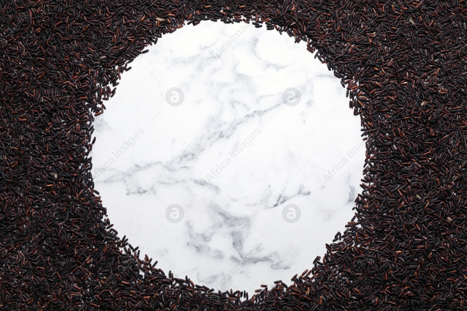 Photo of Frame made of brown rice on white marble table, top view. Space for text