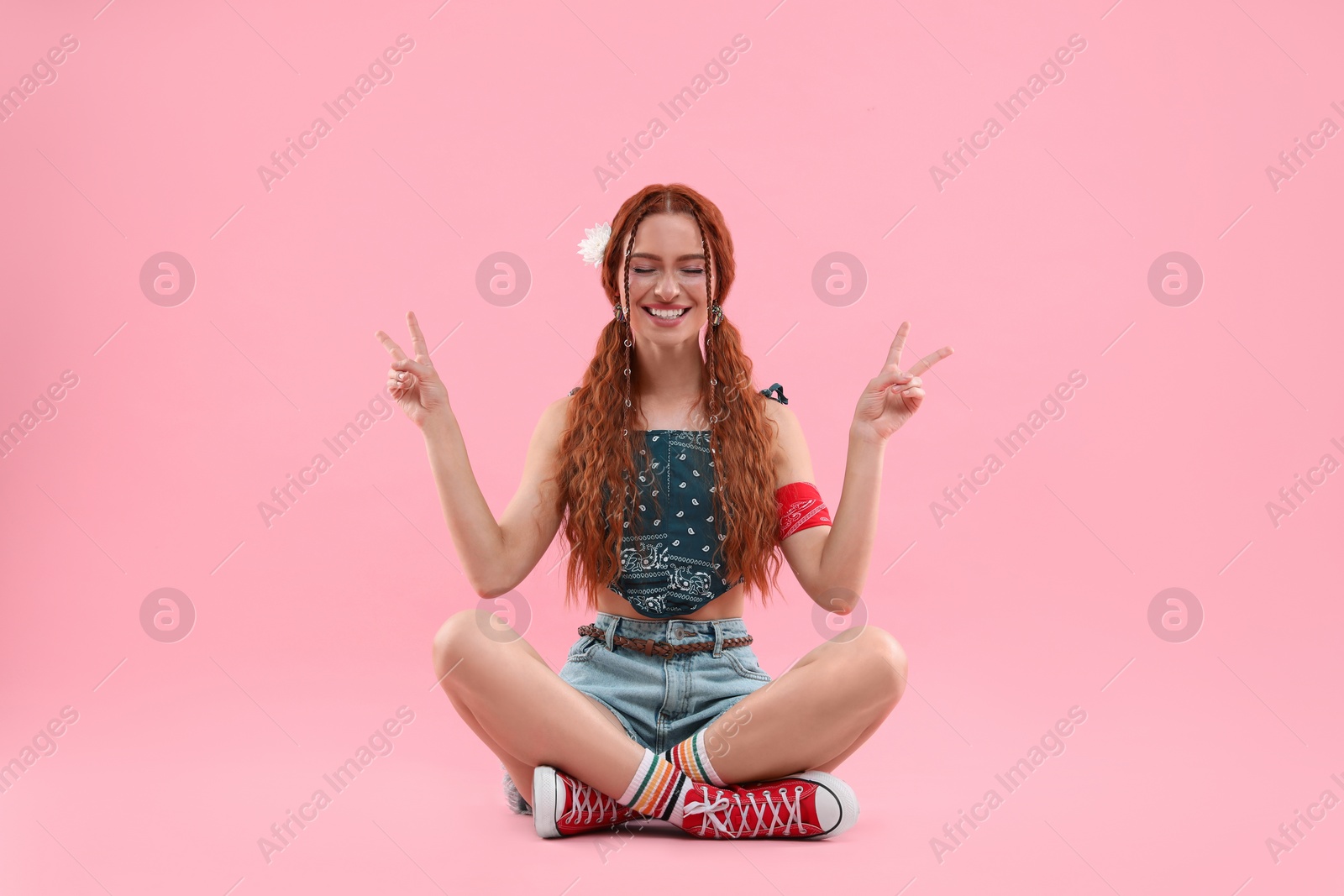 Photo of Beautiful young hippie woman showing V-sign on pink background