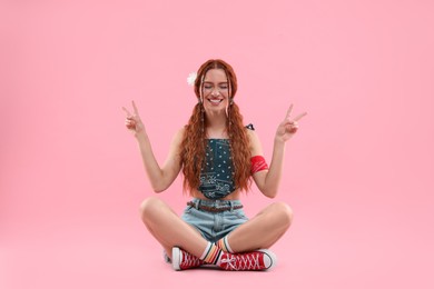 Photo of Beautiful young hippie woman showing V-sign on pink background