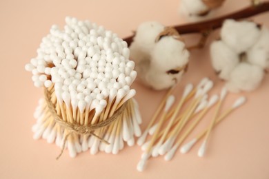 Photo of Many cotton buds and flowers on beige background, closeup