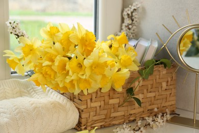 Photo of Beautiful yellow daffodils in wicker basket plum tree branches and mirror on windowsill, closeup