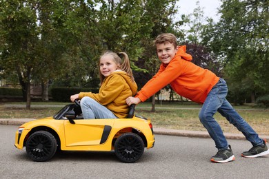 Photo of Cute boy pushing children's car with little girl outdoors