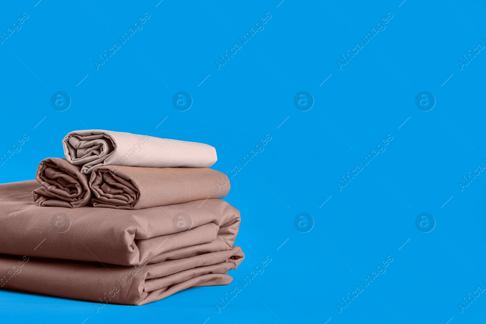 Photo of Stack of clean bed sheets on blue background. Space for text