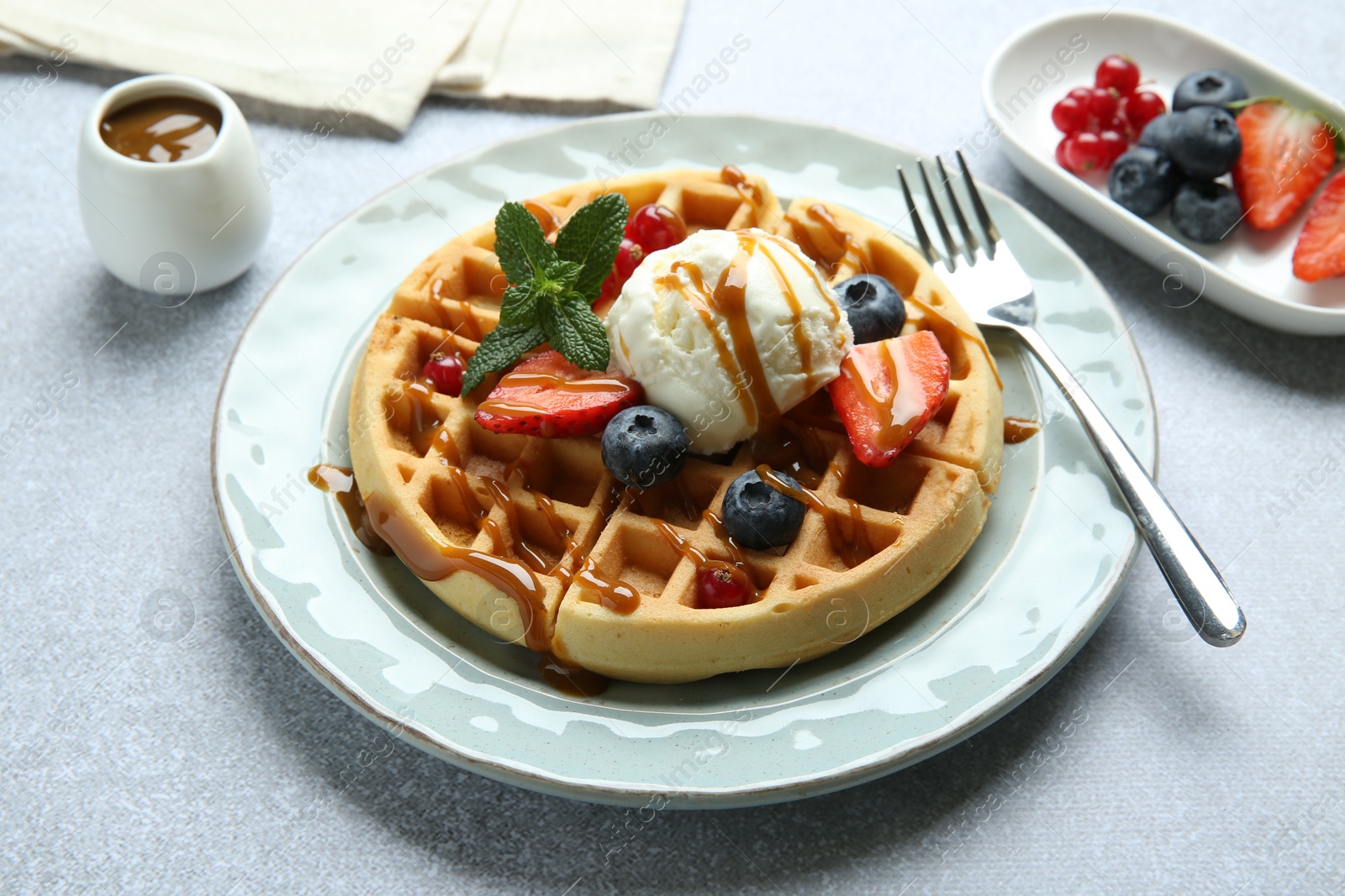 Photo of Delicious Belgian waffles with ice cream, berries and caramel sauce served on grey table, closeup