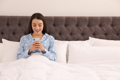 Lonely young woman addicted to smartphone in empty bed at home