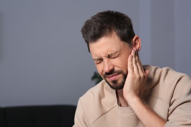 Photo of Man suffering from ear pain on in room, space for text