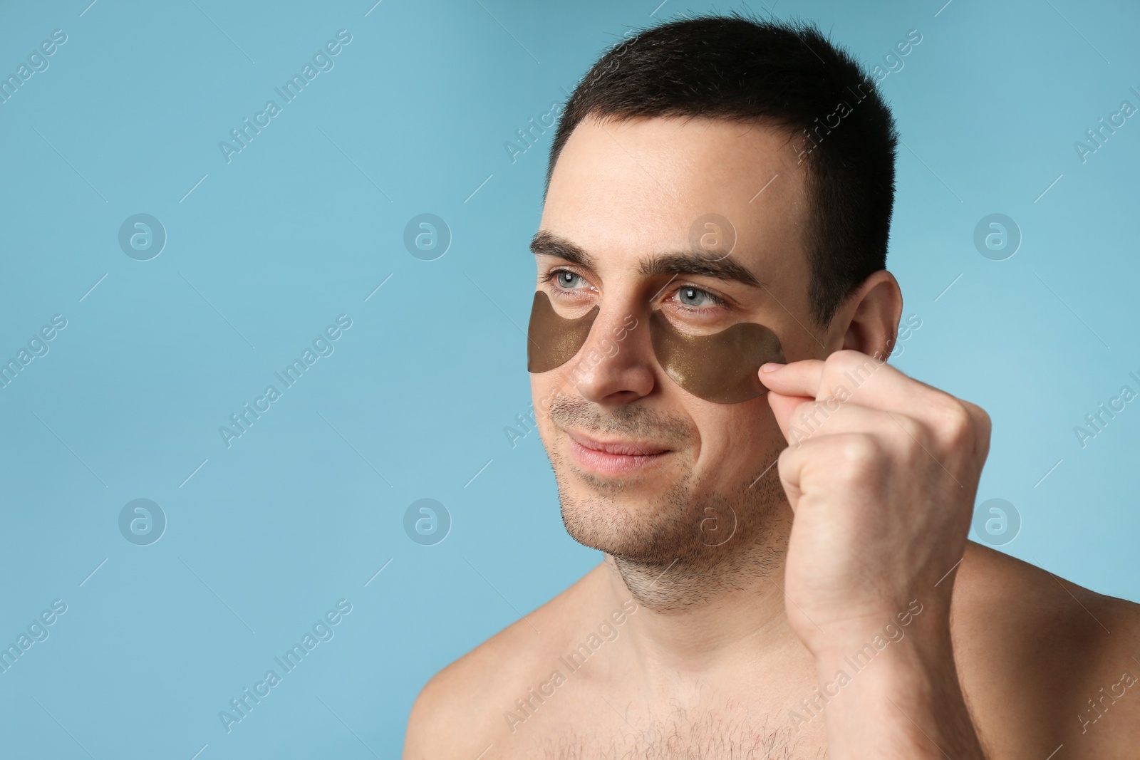 Photo of Young man applying under eye patches on light blue background. Space for text