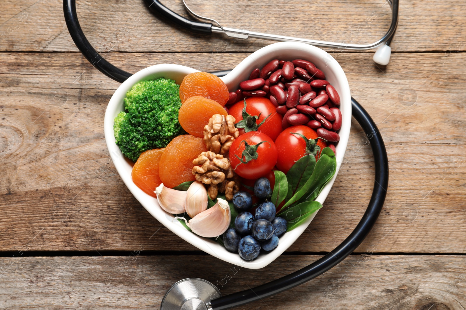 Photo of Bowl with products for heart-healthy diet and stethoscope on wooden background, top view
