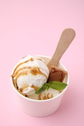 Tasty ice cream with caramel sauce, mint leaves and candy in paper cup on pink table