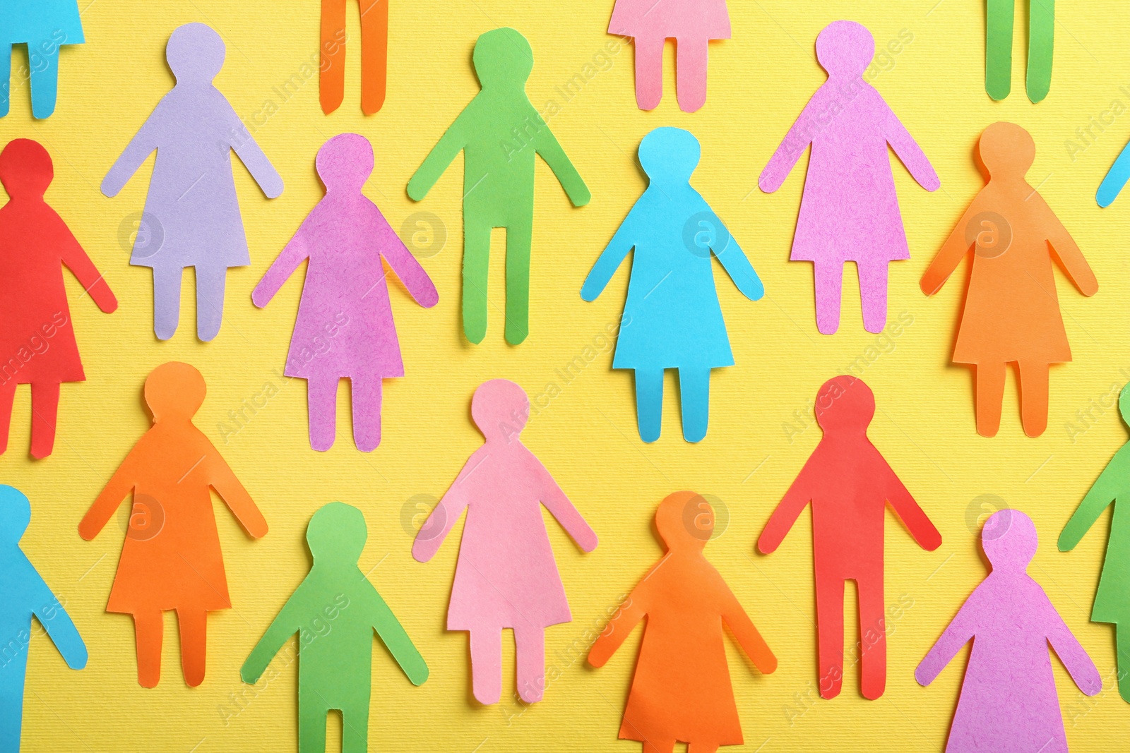 Photo of Many different paper human figures on yellow background, flat lay. Diversity and inclusion concept