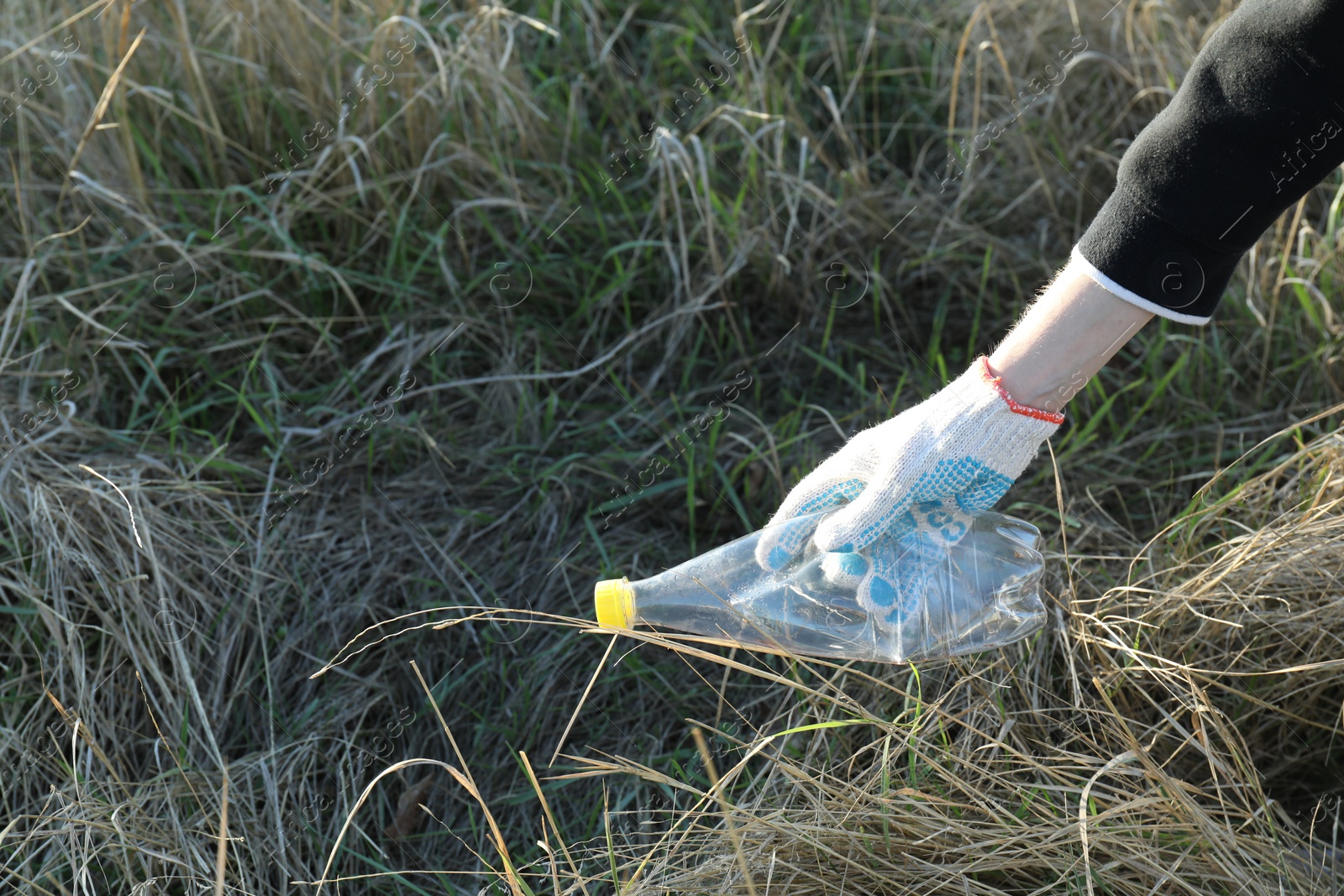 Photo of Woman picking up plastic bottle outdoors, closeup. Space for text