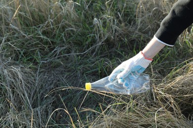 Woman picking up plastic bottle outdoors, closeup. Space for text