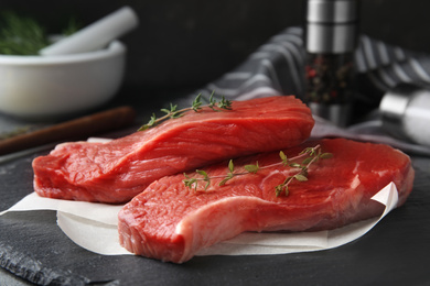 Photo of Fresh raw beef cut with thyme on black table, closeup