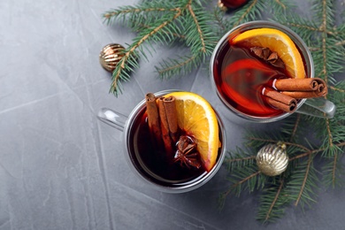 Glass cups with mulled wine and fir branches on grey table, flat lay
