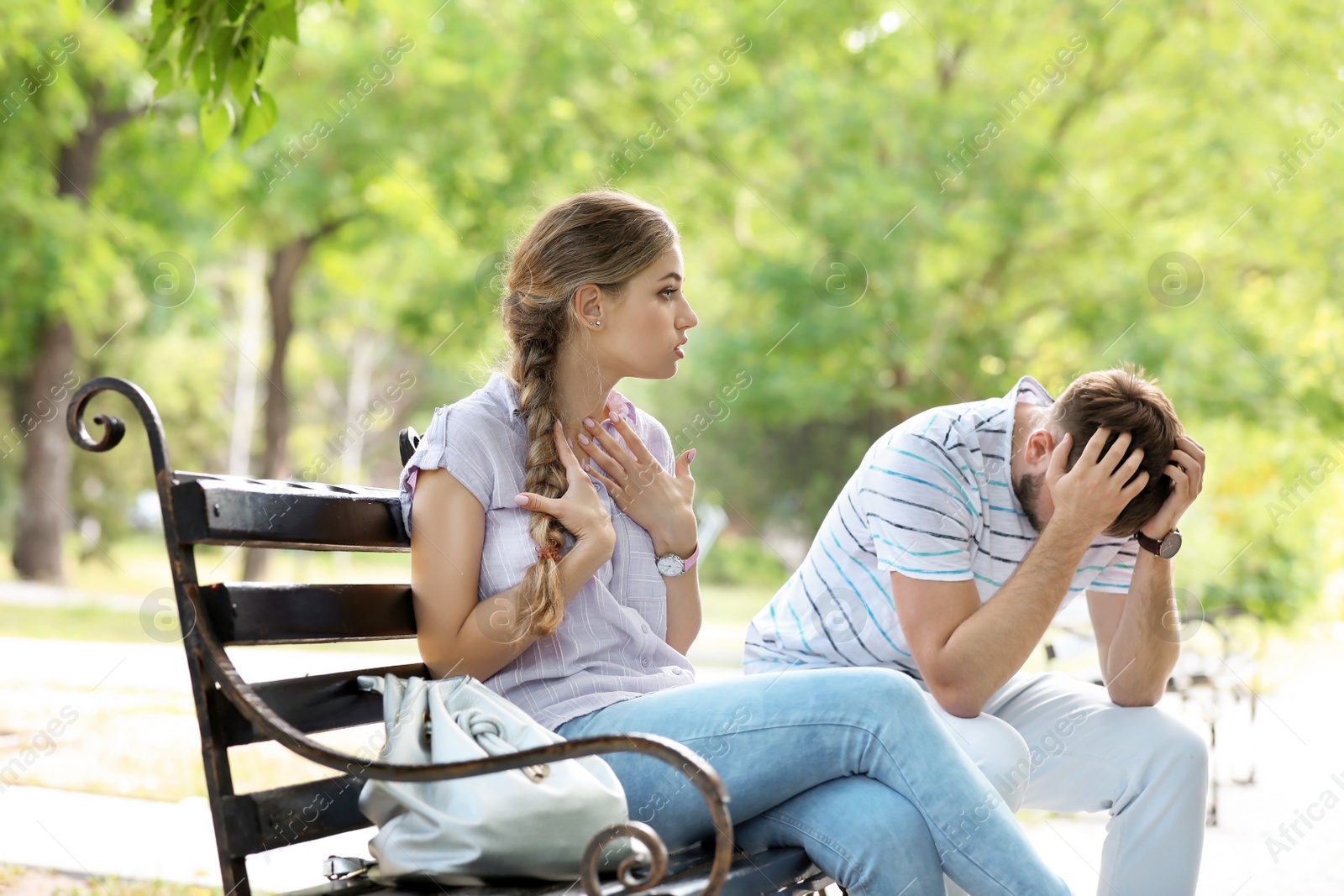 Photo of Young couple arguing while sitting on bench in park. Problems in relationship