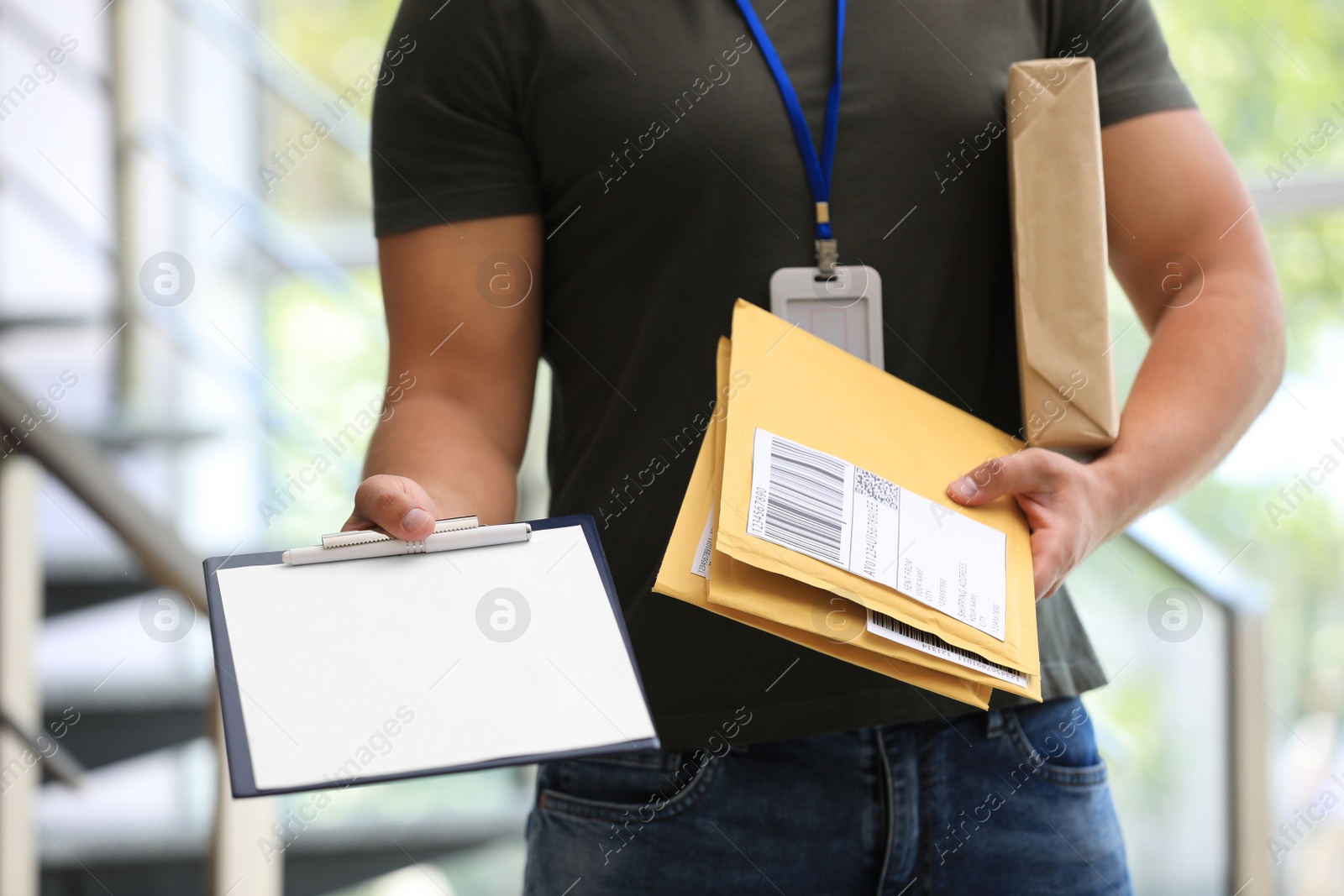 Photo of Young courier with parcels and clipboard indoors, closeup. Delivery service
