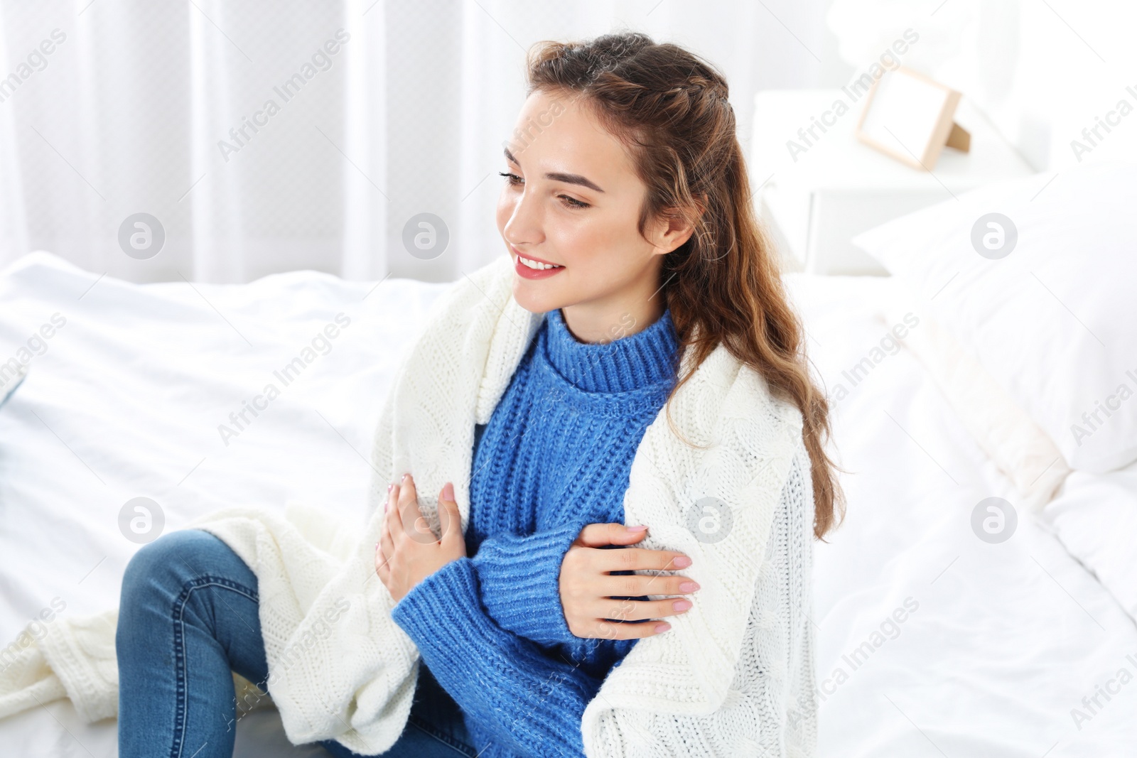 Photo of Beautiful teenage girl in warm cozy sweater with plaid sitting on bed at home