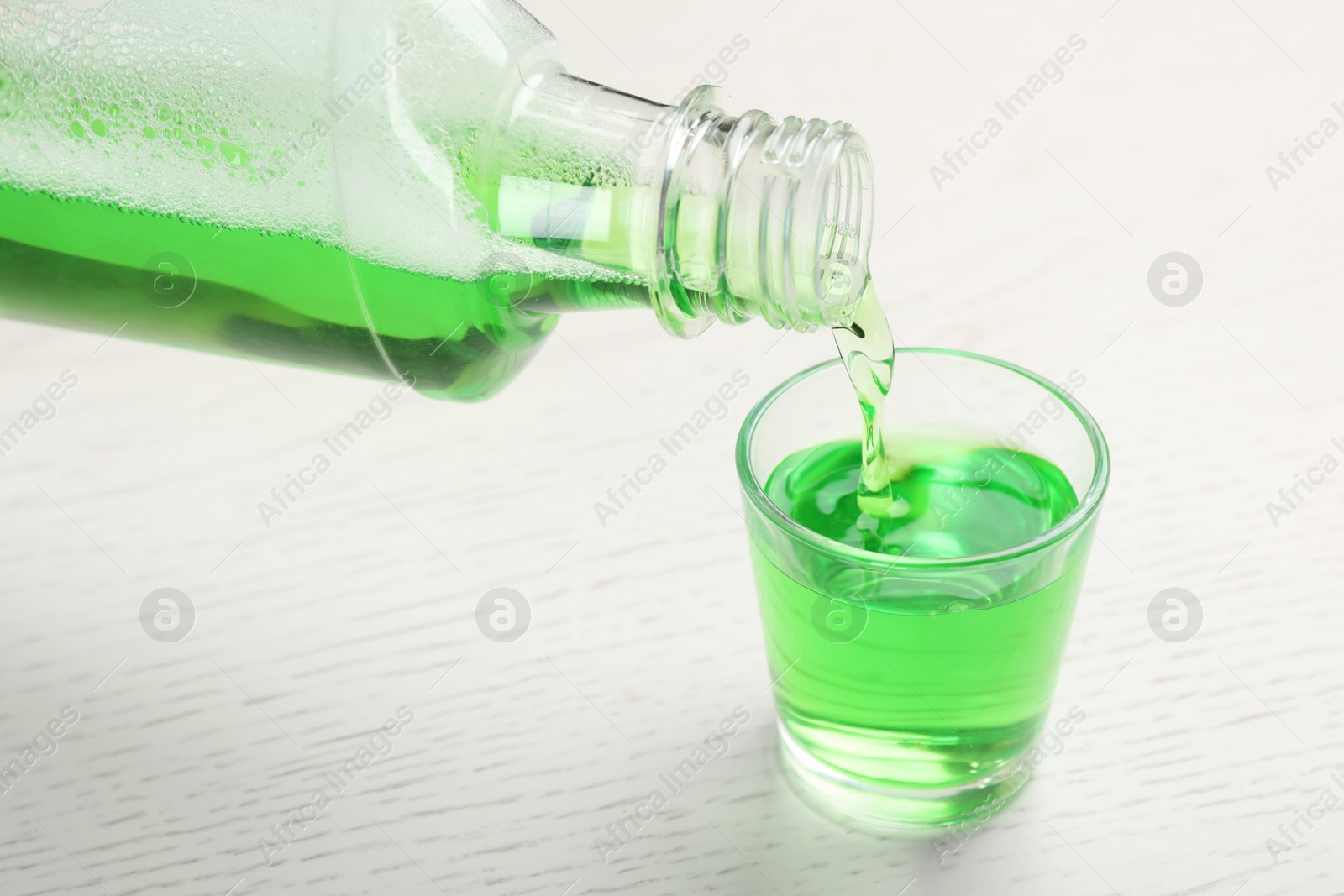 Photo of Pouring mouthwash in glass on wooden background. Teeth care