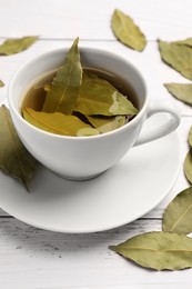 Cup of freshly brewed tea with bay leaves on white wooden table, closeup