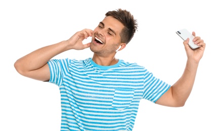 Happy young man with smartphone listening to music through wireless earphones on white background