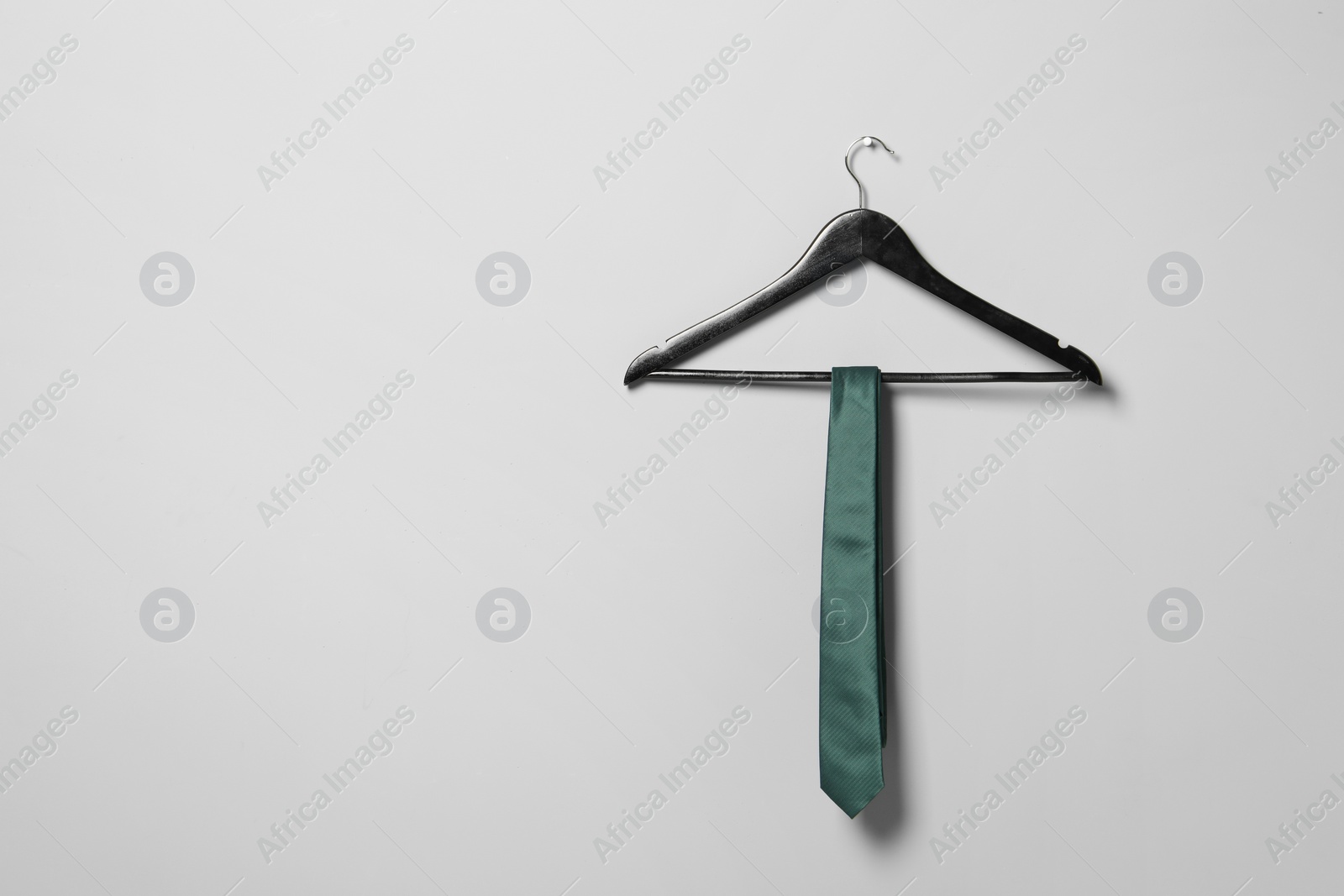 Photo of Hanger with green necktie on light grey wall. Space for text