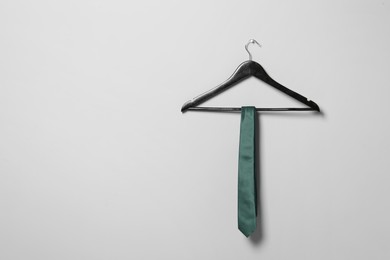 Hanger with green necktie on light grey wall. Space for text