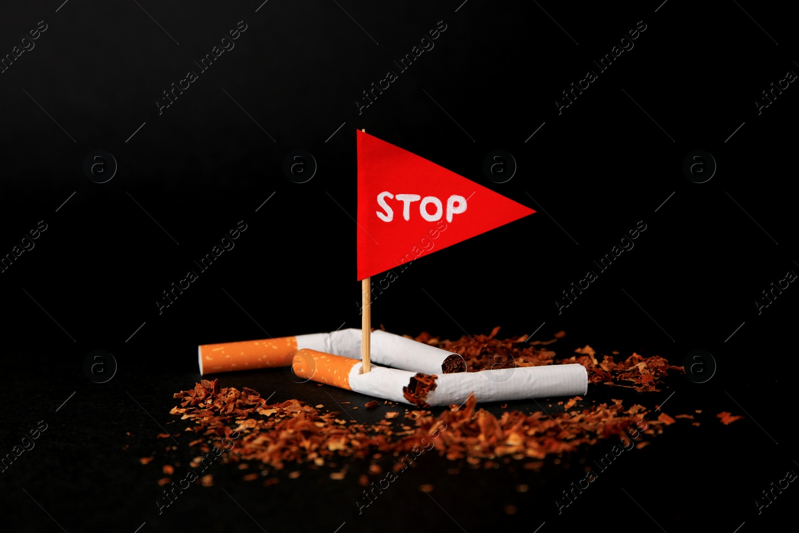 Photo of Broken cigarettes and red flag with word Stop on black background, closeup. Quitting smoking concept