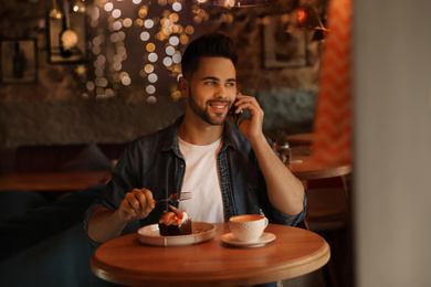 Photo of Young blogger talking on phone at table in cafe