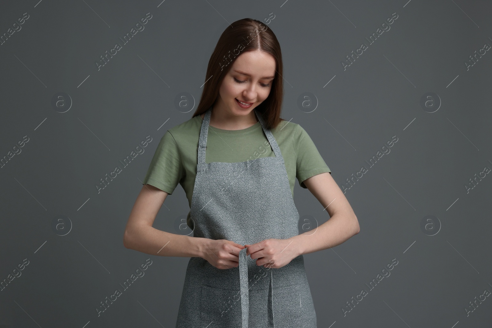 Photo of Beautiful young woman wearing kitchen apron on grey background. Mockup for design