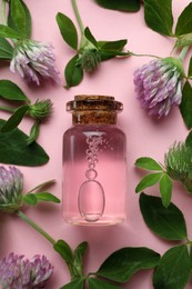 Photo of Beautiful clover flowers and bottle of essential oil on pink background, flat lay