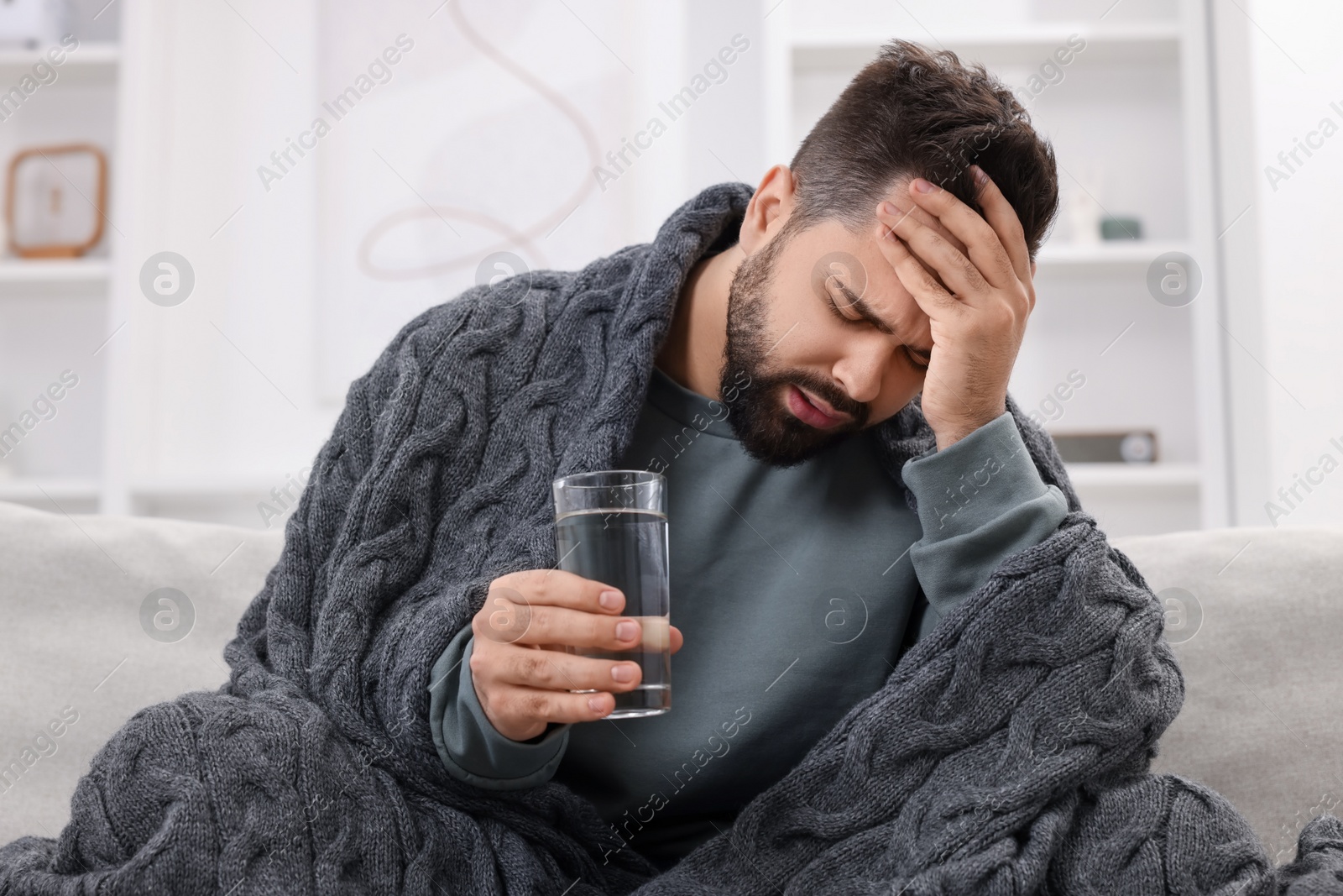 Photo of Man with glass of water suffering from headache on sofa at home