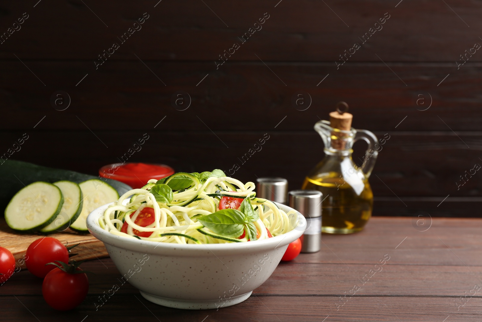 Photo of Delicious zucchini pasta with cherry tomatoes and basil in bowl on wooden table. Space for text