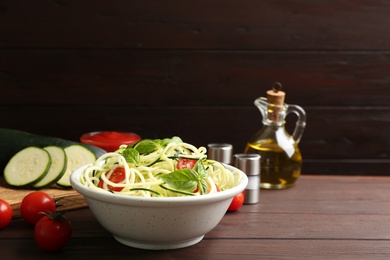 Delicious zucchini pasta with cherry tomatoes and basil in bowl on wooden table. Space for text