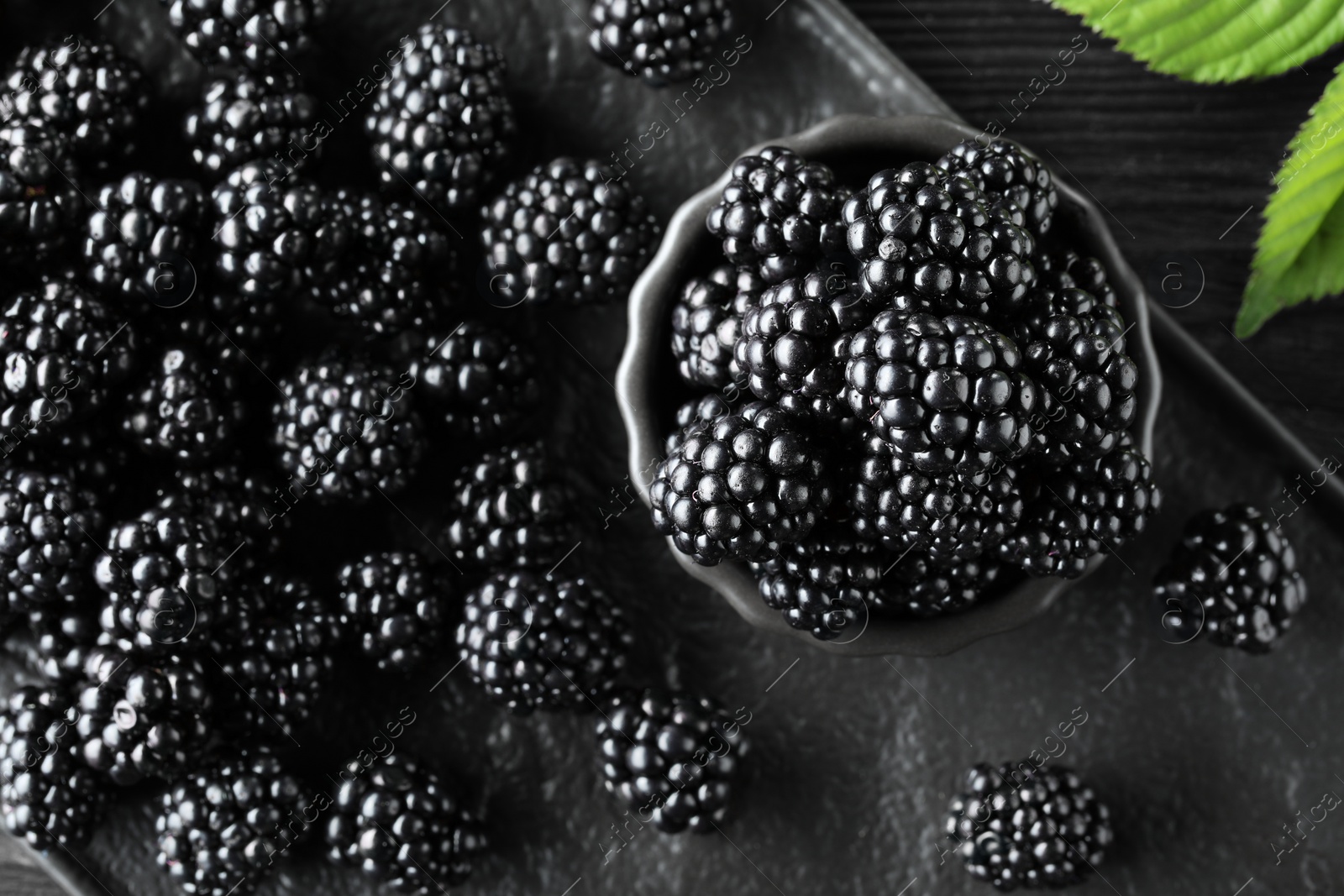 Photo of Fresh ripe blackberries and leaves on black board, flat lay