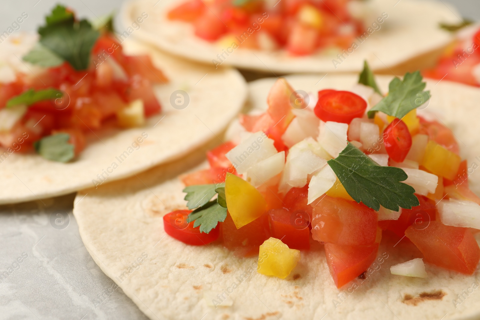 Photo of Delicious tacos with vegetables and parsley on grey table, closeup