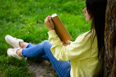 Young woman reading book near tree in park