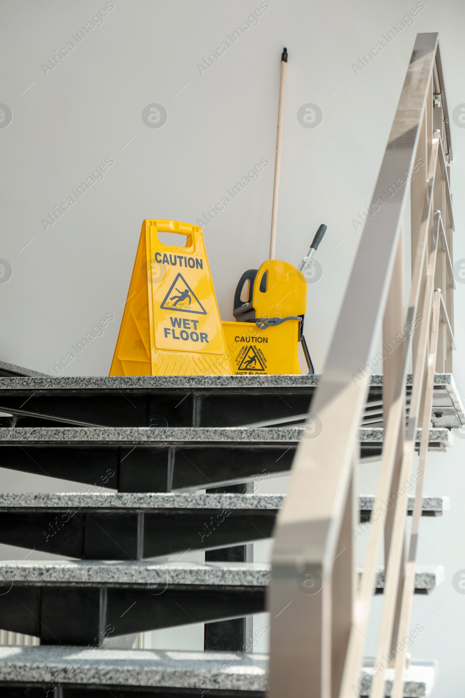 Photo of Safety sign with phrase Caution wet floor and mop bucket on stairs. Cleaning service