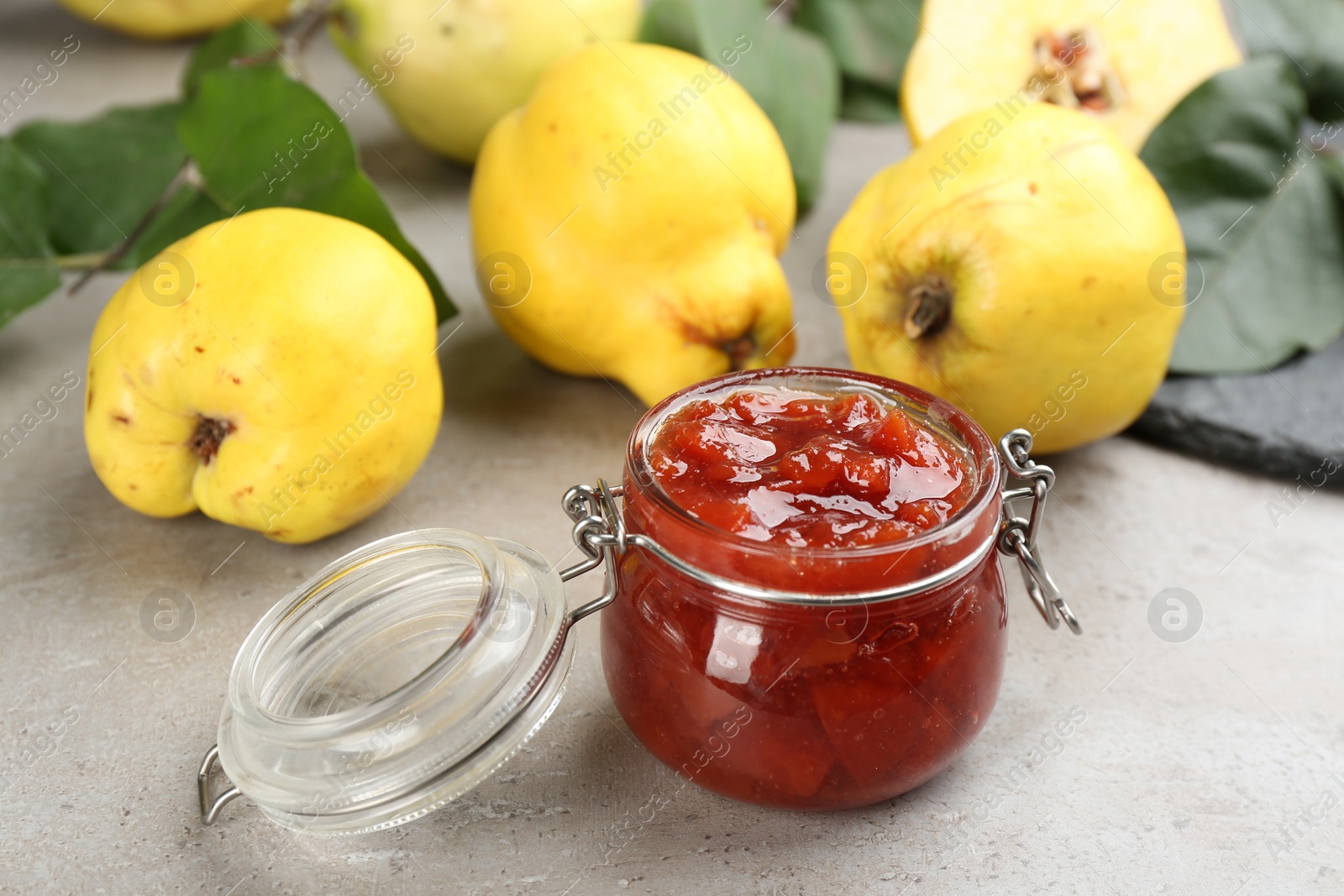 Photo of Delicious quince jam and fruits on light grey table, closeup