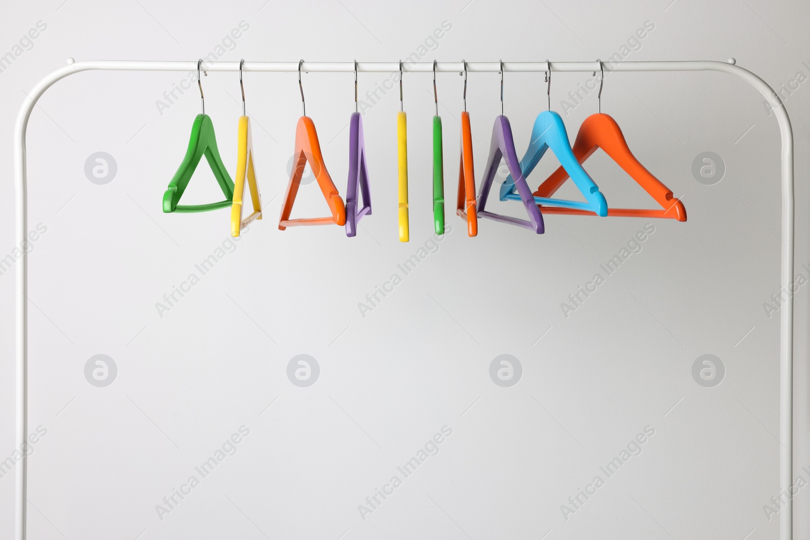 Photo of Bright clothes hangers on metal rack against light background