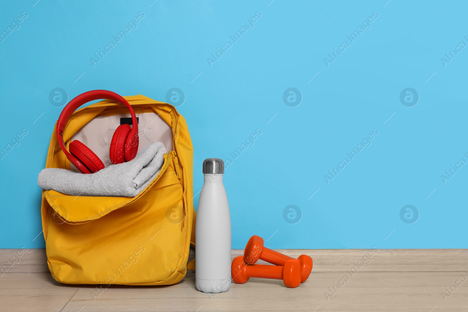 Photo of Backpack and sports equipment on floor near light blue wall, space for text