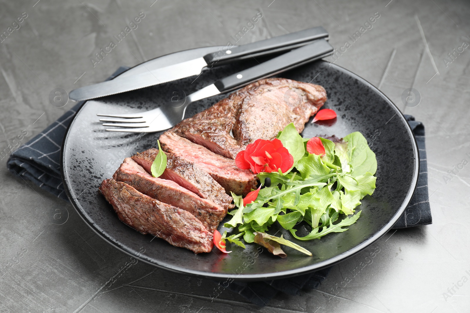 Photo of Delicious grilled beef meat served with greens on grey table