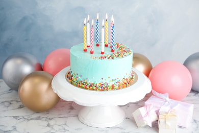 Fresh delicious birthday cake, gifts and balloons on table against color background