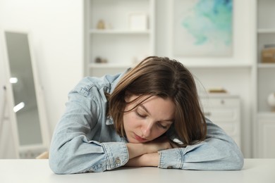 Photo of Sad young woman sitting at white table in room