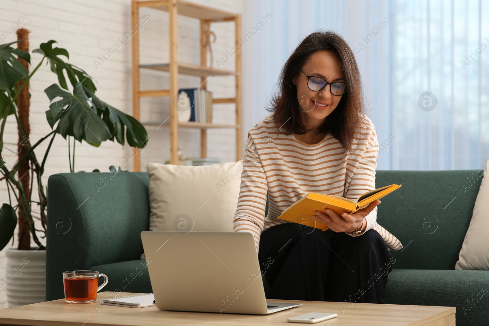 Photo of Woman with modern laptop and book learning in living room