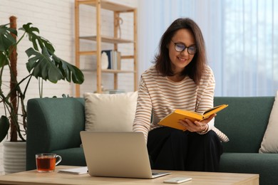 Photo of Woman with modern laptop and book learning in living room